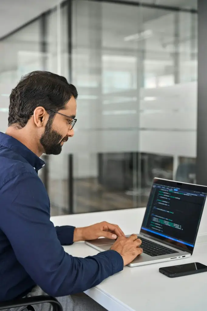 Indian business man software developer working on laptop in office. Vertical